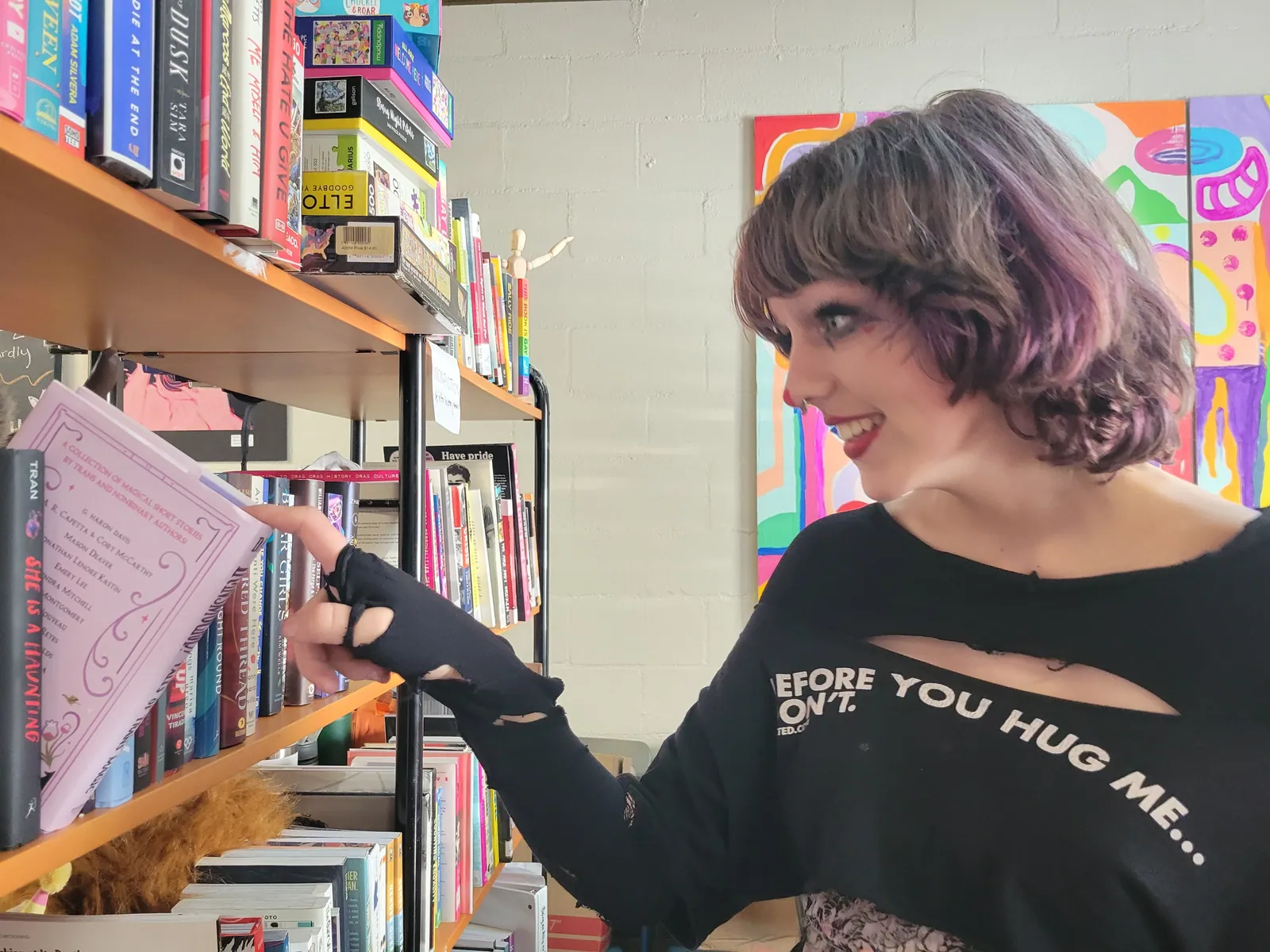 A young person with purple streaked hair pulling a book from a shelf in the youth library.