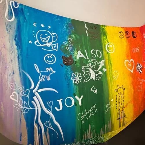 The finished rainbow car hood, covered in white drawings and words: ALSO, JOY, Celebrate Life, You Matter, Stand Tall, We Believe in You, a smiling sun, a cat, a giraffe, and hearts.