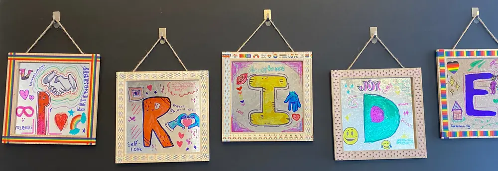 Five framed mirrors, each decorated with one letter of PRIDE and words like friends, self-love, acceptance, joy, and community.
