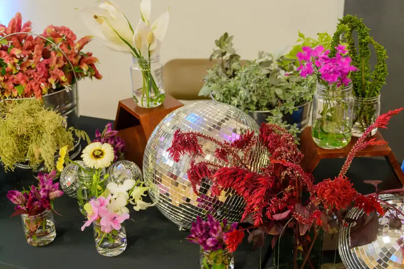 Prom 2023 table decor: bright flowers in small glass vases around mirrored disco balls.