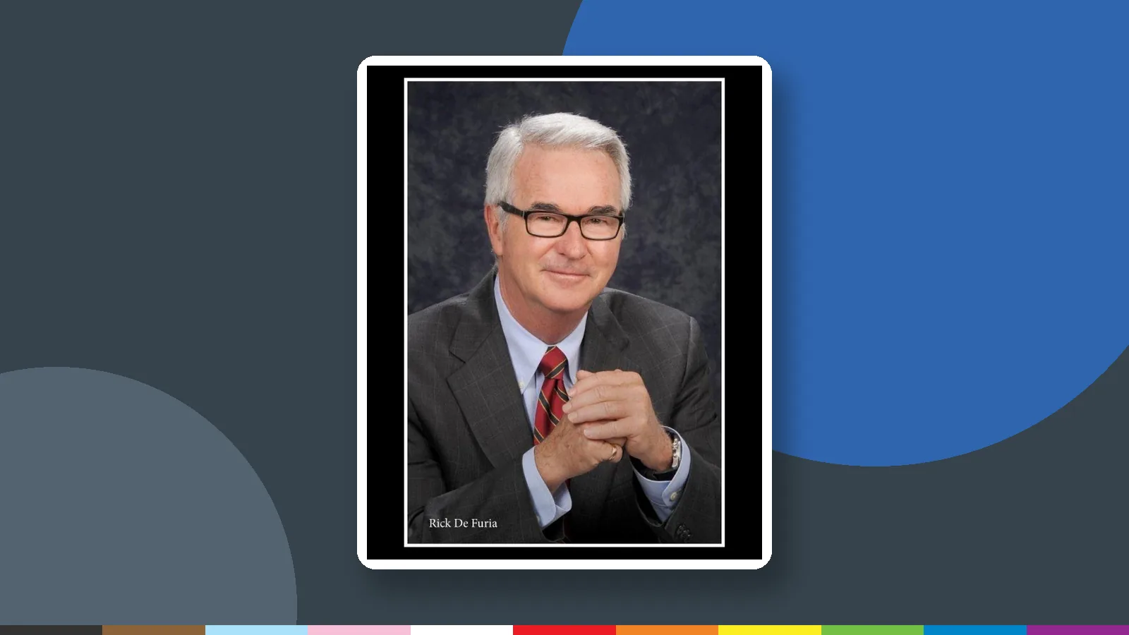 Studio portrait of Judge Rick De Furia in a suit and red tie, set in a white frame on a slate and blue panel.