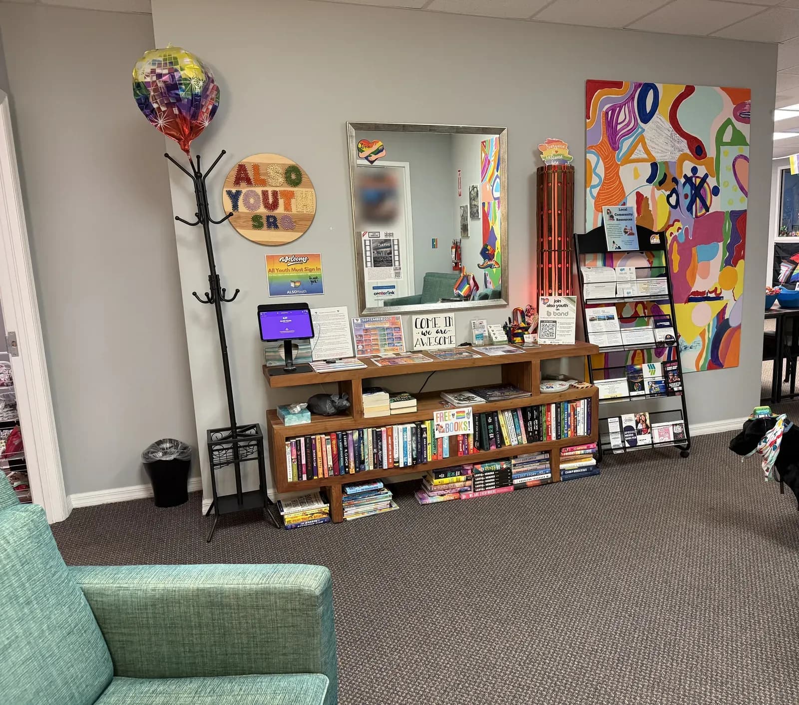 The welcome area at the Sarasota Center: an ALSO Youth SRQ sign, a sign in tablet, free books, resource flyers, and a bright painted mural.