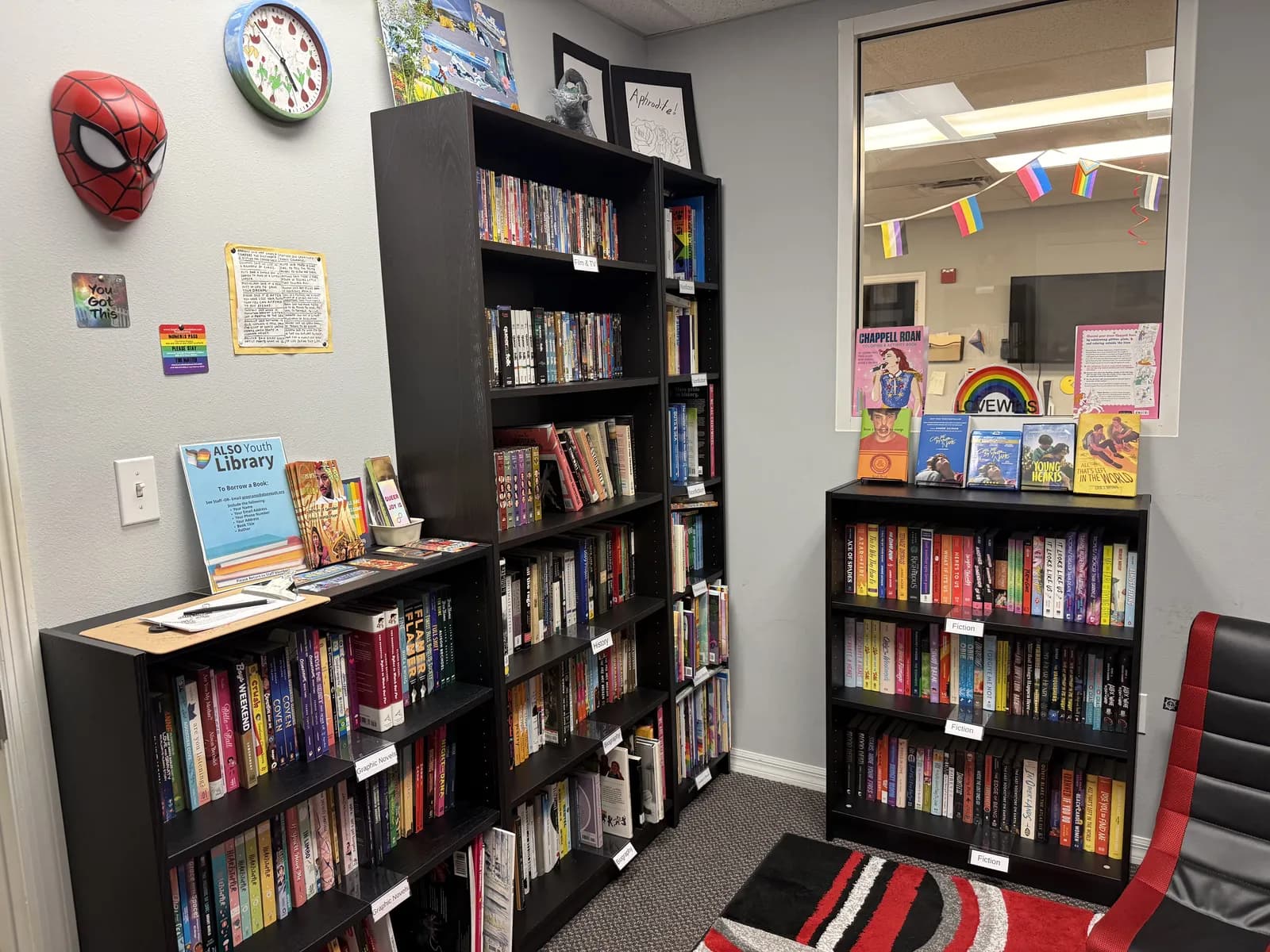 The library corner at the Sarasota Center: black bookshelves, a Spider-Man mask and a clock on the wall, and a comfy red chair.