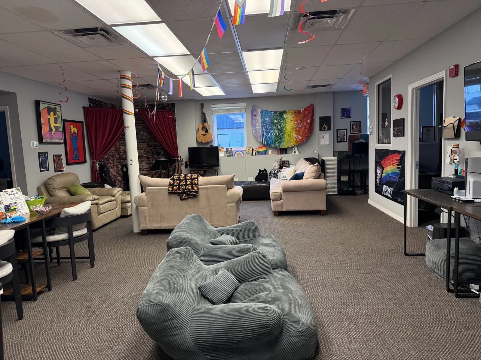 The youth lounge at the Sarasota Center: couches, big bean bags, a guitar on the wall, pride flag bunting, and a rainbow painted art piece.