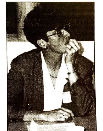 Newspaper photo of Betsy Nelson, a founder of ALSO Youth, seated at a panel table with her hand at her chin.