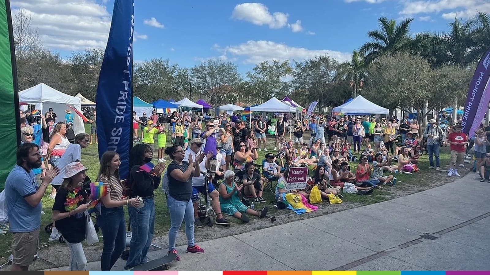 Hundreds of people on the lawn at Manatee Pride 2022 at Bradenton Riverwalk, among white vendor tents and Pride banners.