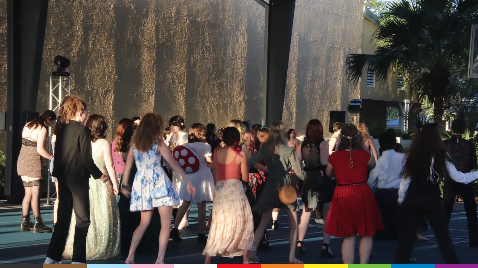 Young people in formal wear dance together outdoors at an ALSO Youth event, seen from behind.
